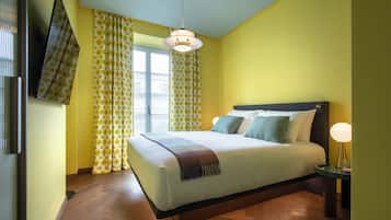 A bedroom with a bed, curtains, a hanging light fixture, and a bedside table.