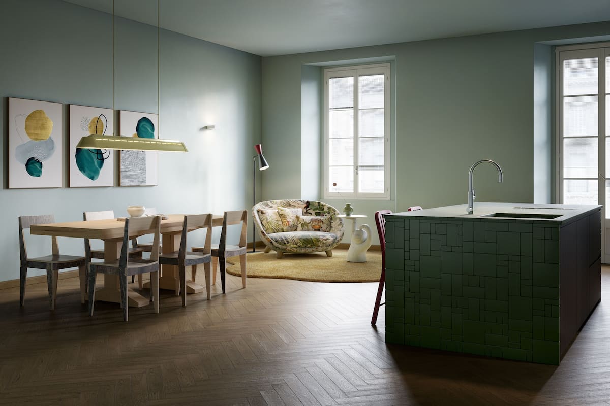 Une cuisine moderne avec un îlot central vert, une table à manger en bois et des chaises. On y trouve une fenêtre avec des stores et un luminaire suspendu.