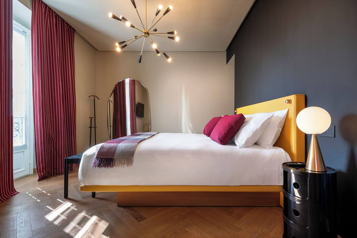 Une chambre à coucher moderne avec un grand lit, un luminaire au plafond original et une table de chevet avec une lampe.