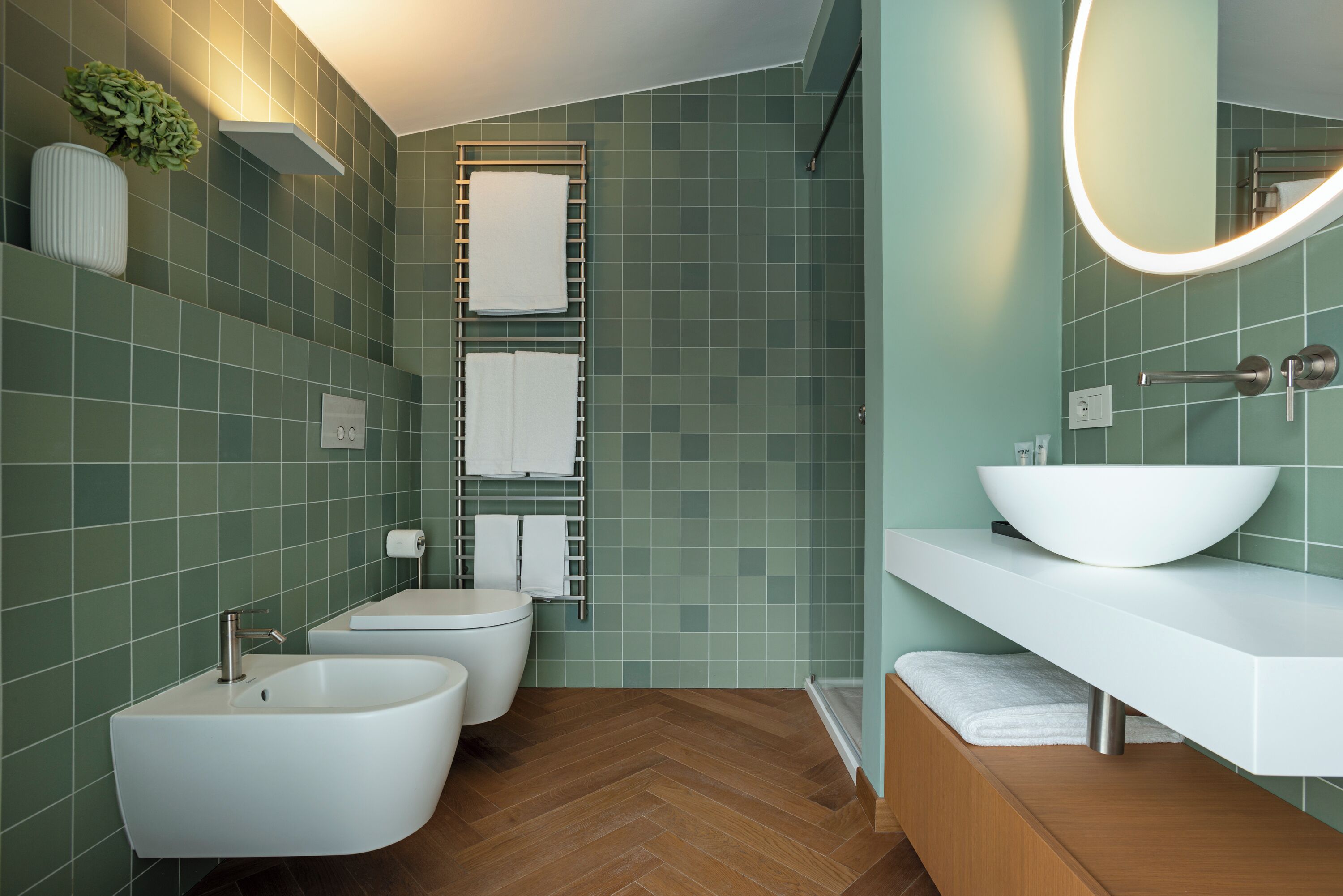 Une salle de bain avec un lavabo blanc, deux bidet, des toilettes et un miroir avec un éclairage intégré.