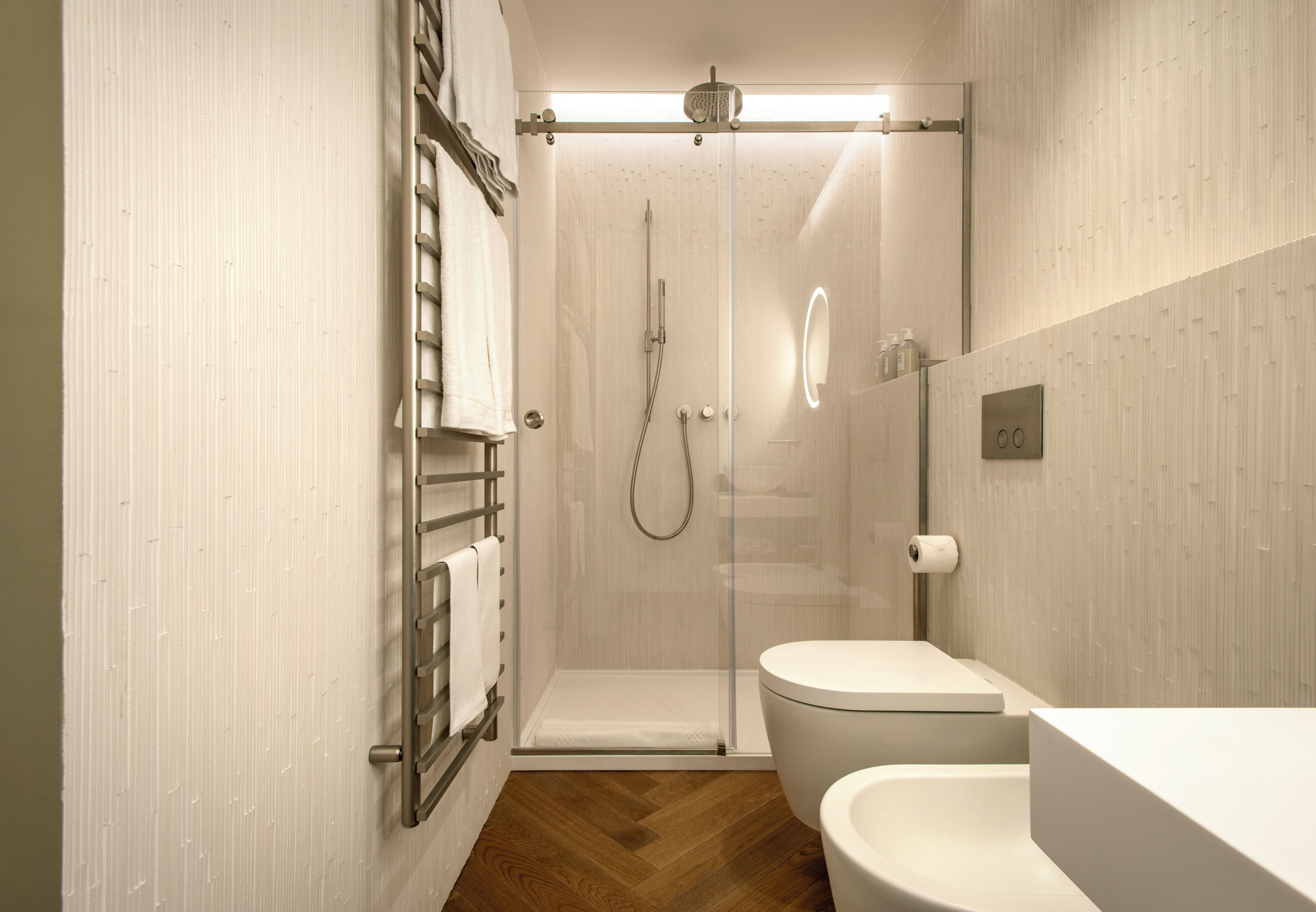 Ein modernes Badezimmer mit einer gläsernen Duschkabine, einer weißen Toilette und einem Holzboden.