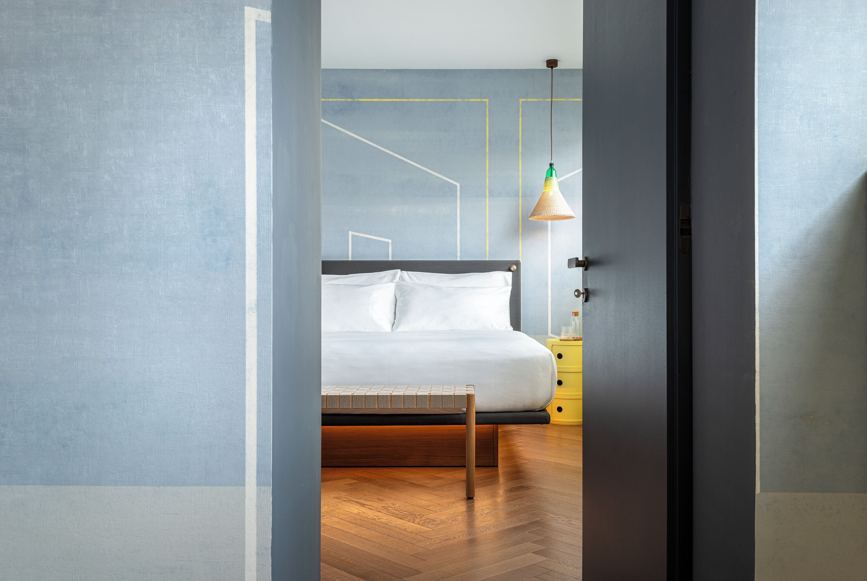 A bedroom with a bed, wooden floor, and a yellow nightstand.