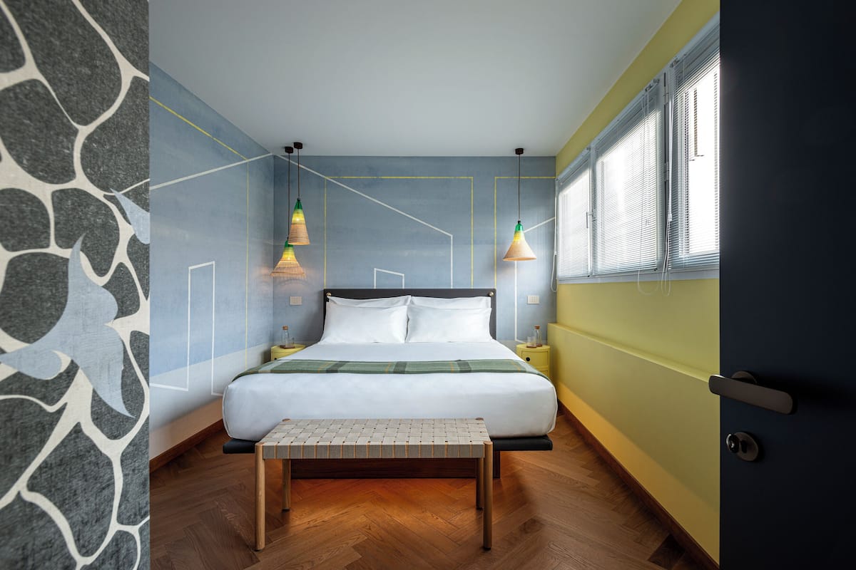 Une chambre à coucher avec un lit, des tables de chevet, un banc et une fenêtre avec des stores.
