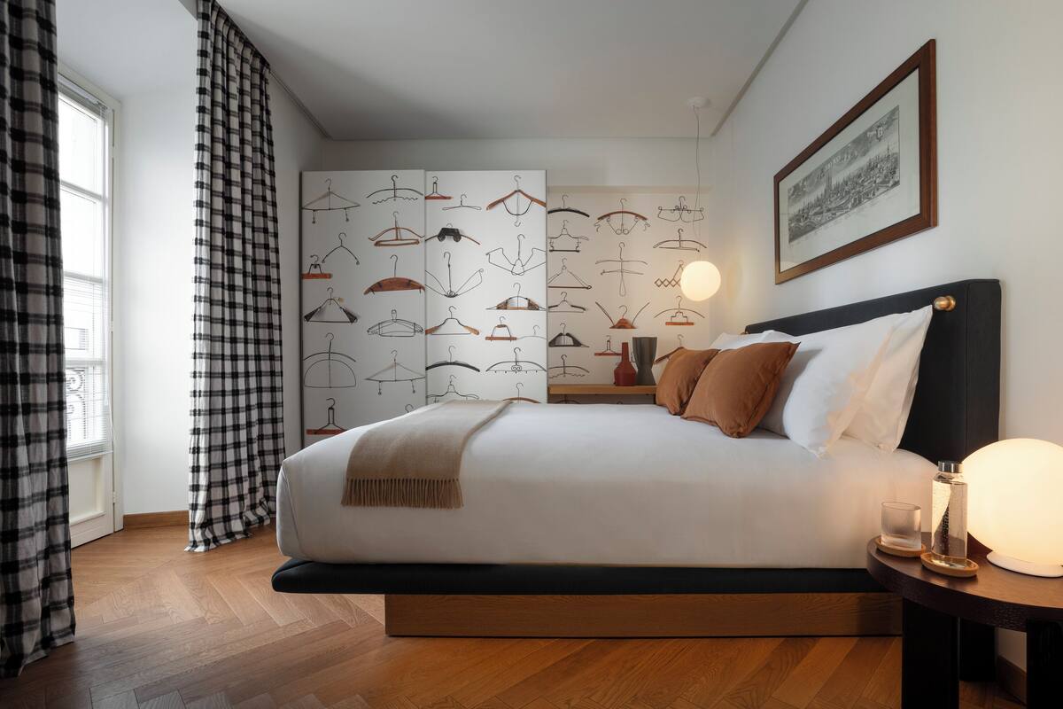 Un lit bien fait, avec une tête de lit, une table de chevet avec une lampe et un mur sur lequel est accroché un portant à vêtements.