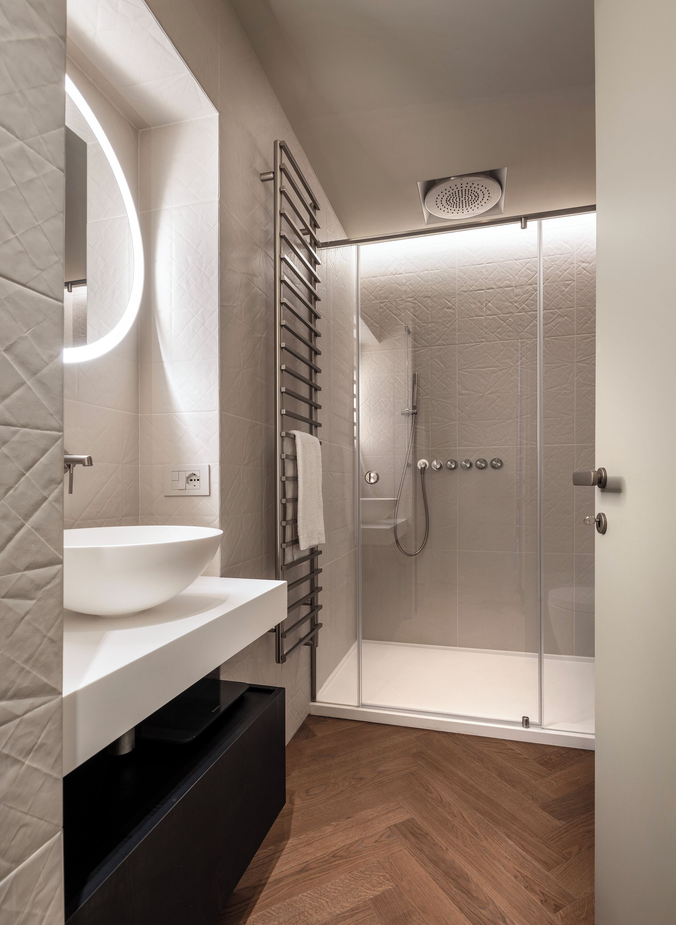 Un bagno moderno con un lavandino spazioso, cabina doccia in vetro e pavimento in legno.