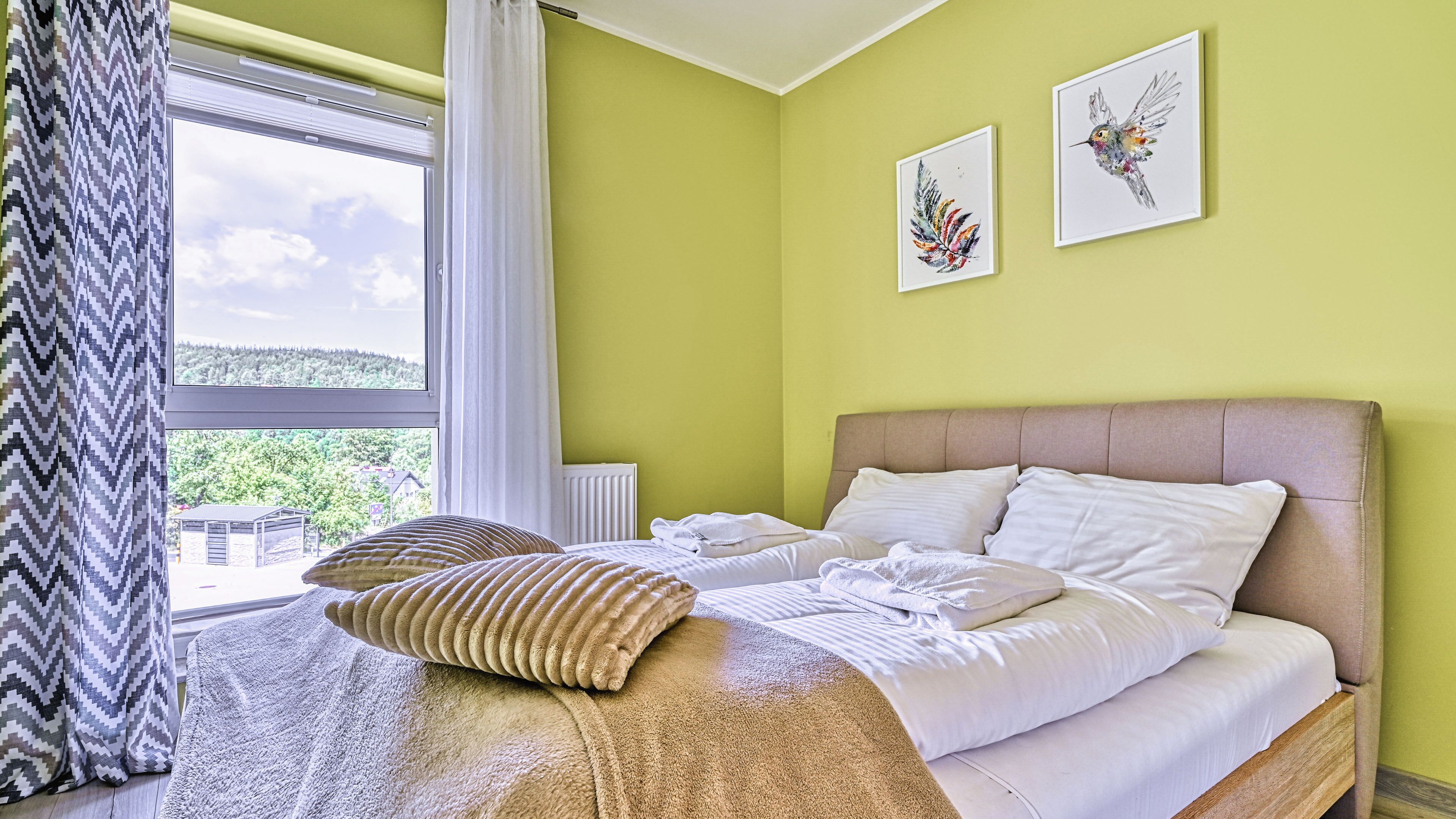 A bedroom with a bed, pillows, a window with curtains, and two framed pictures on the wall.