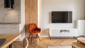 Un salon moderne doté d’un téléviseur, de planchers en bois, d’un meuble de rangement blanc et d’un coin repas avec une table et des chaises.