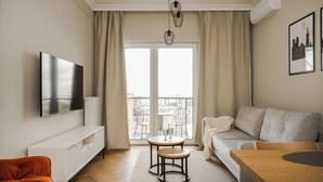 Un salon moderne doté d’un téléviseur à écran plat, d’un canapé, d’une table en bois et d’un balcon offrant une vue sur les immeubles.
