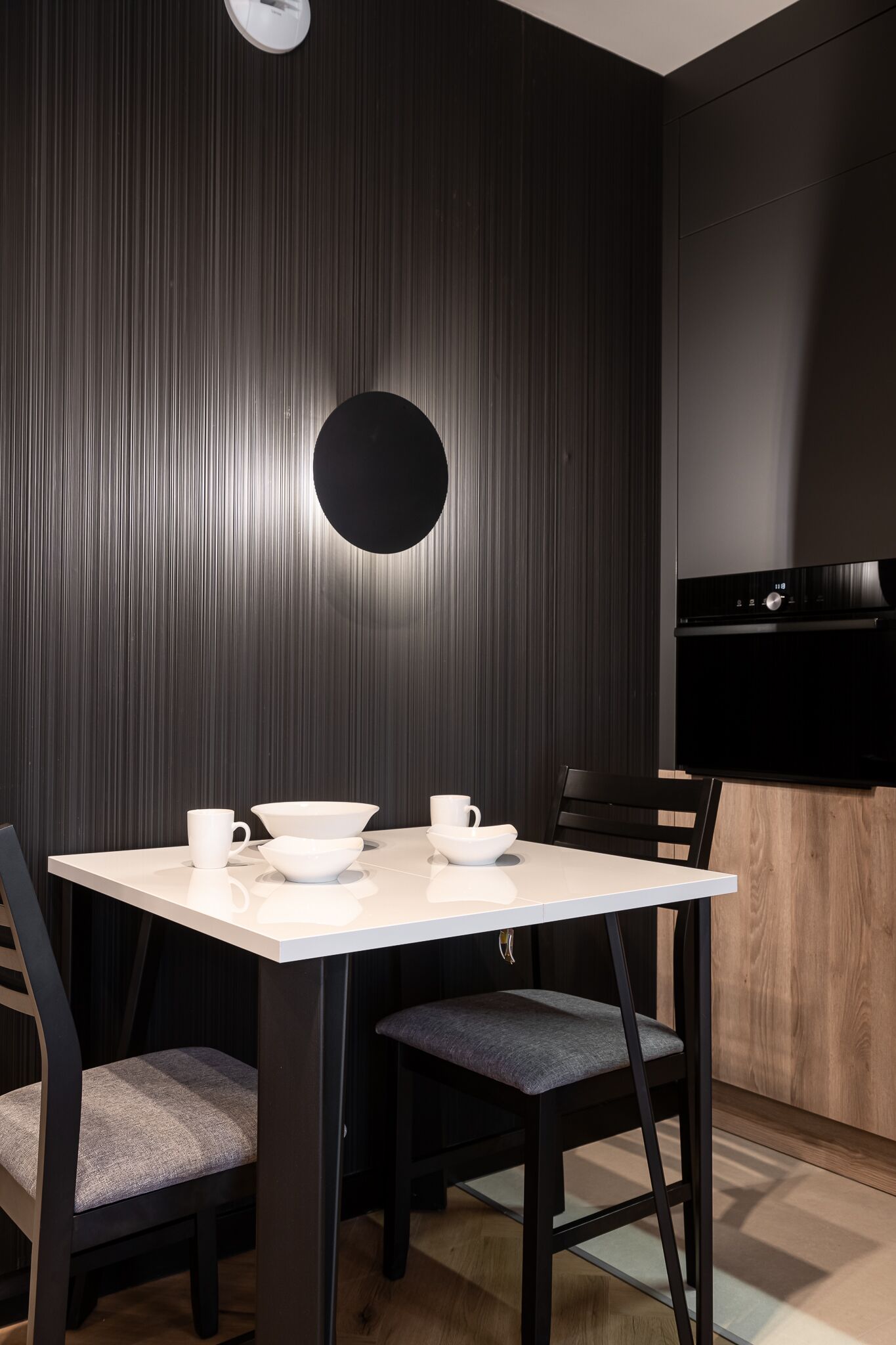 Zona pranzo moderna con un tavolo rettangolare, quattro sedie e una parete nera con linee verticali.