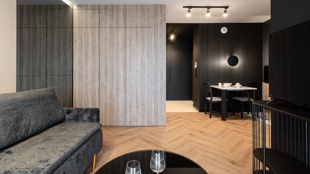 Un salon moderne avec un canapé gris, un coin repas comprenant une table et des chaises, et un téléviseur posé sur un meuble noir.