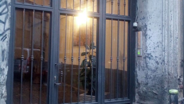 Un'ampia cancello in metallo scuro, con sbarre verticali e un finestrone ad arco sopra, incastonato in una porta arcuata.