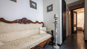 Un corridoio con pavimento in legno, un divano con cuscino decorato e una lampada alta.