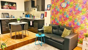 A modern kitchen with a dining area, a black leather sofa, and a colorful brick wall. - Rainbow Studio - Spacious City Centre - Close to sea - Sleeps 1 to 3 Guests (Brighton)