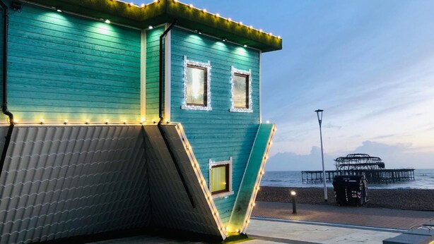 A teal building with two windows, a slanted roof, and a dock extending into the water. - Rainbow Studio - Spacious City Centre - Close to sea - Sleeps 1 to 3 Guests (Brighton)