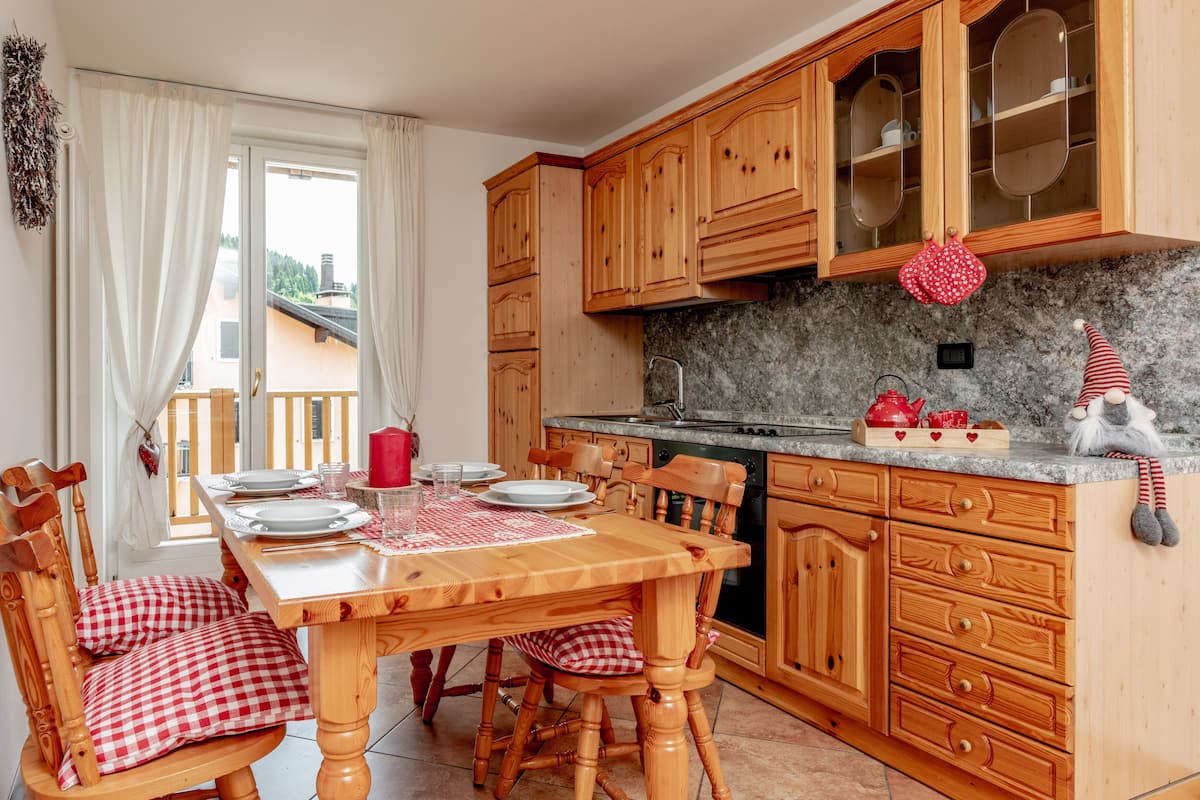 Une cuisine avec des meubles en bois, un plan de travail en granit et une table à manger dressée avec des assiettes et une nappe à carreaux rouges.
