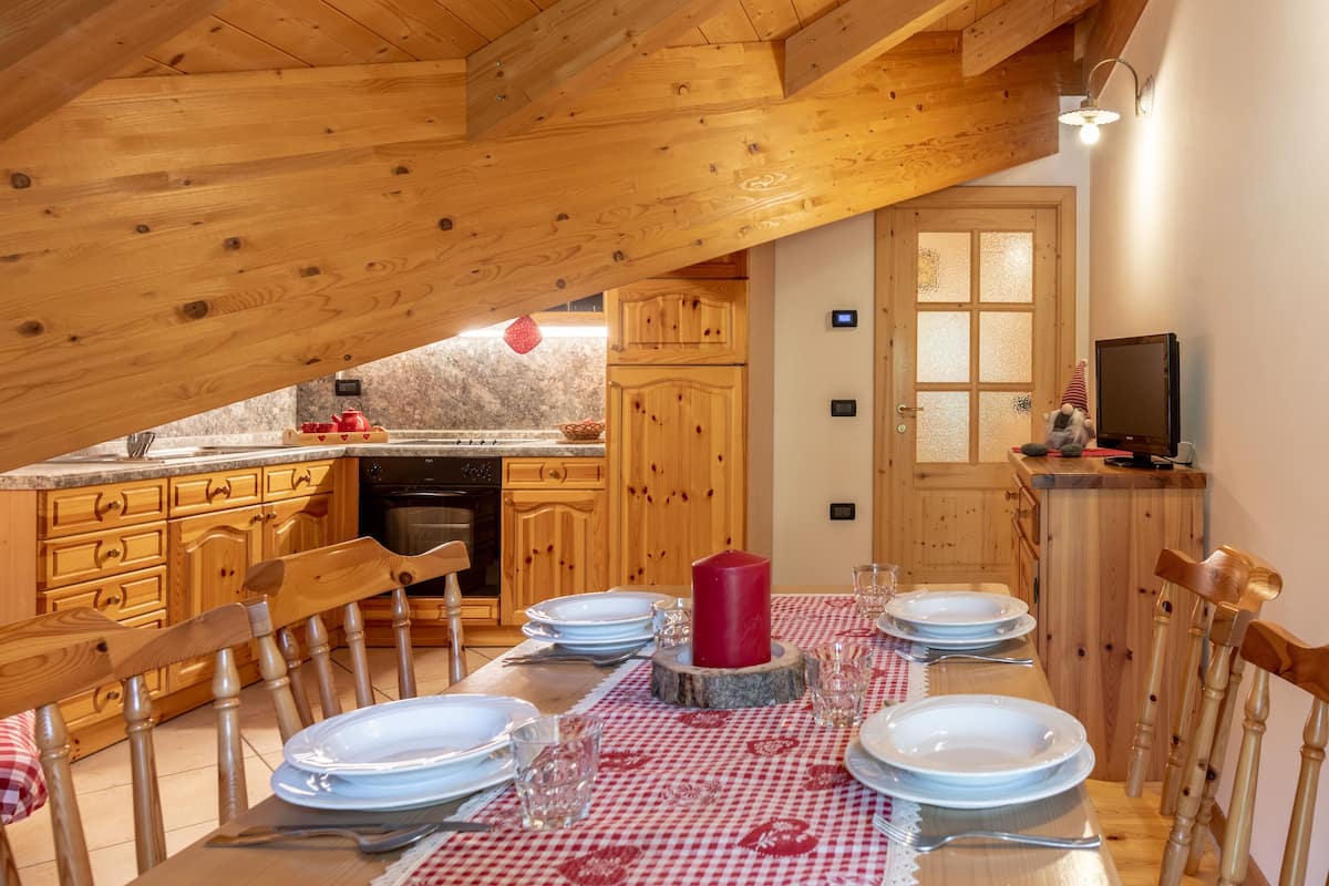 Un coin repas en bois avec une table dressée pour quatre personnes, un chandelier rouge comme décoration centrale et des chaises en bois.