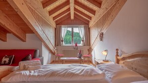A cozy bedroom with a wooden ceiling, a large bed, a window with curtains, a small table, and a nightstand with a lamp. - RESIDENCE STELLA (Folgaria)