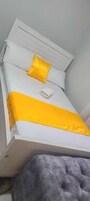 A bed with white bedding and a yellow accent pillow, a grey upholstered bench, and a white headboard.