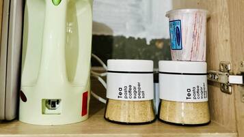 A kitchen with a coffee maker, two spice jars labeled tea, pasta, coffee, sugar, pepper, and salt, and a measuring cup.
