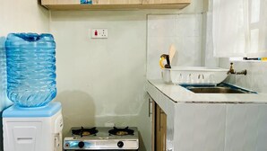 Una cocina compacta con estufa a gas, dispensador de agua y lavamanos.