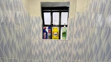 Un baño con inodoro, una ventana y tres botellas de productos de limpieza en el alféizar.