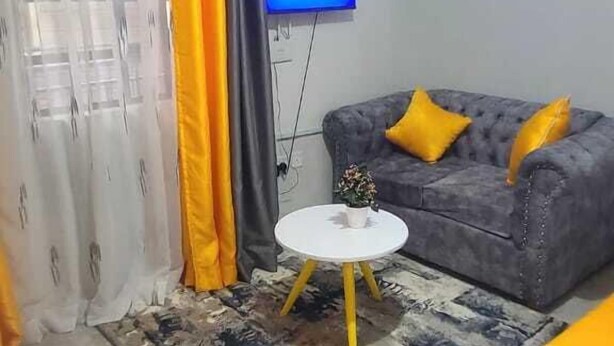 Un salón con un sofá gris, cojines amarillos, una mesita blanca y un televisor en la pared.