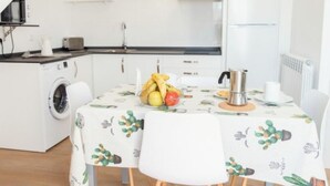 A modern kitchen with a washing machine, a dining table with a cactus-patterned tablecloth, and a fruit bowl. - Apartment - 2 Bedrooms - 8951 (La Aparecida, Cantabria)