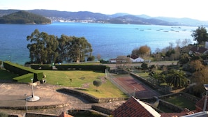 Weitläufige Küstenlandschaft mit Tennisplatz, angelegten Gärten und einem Wasserabschnitt mit Booten.