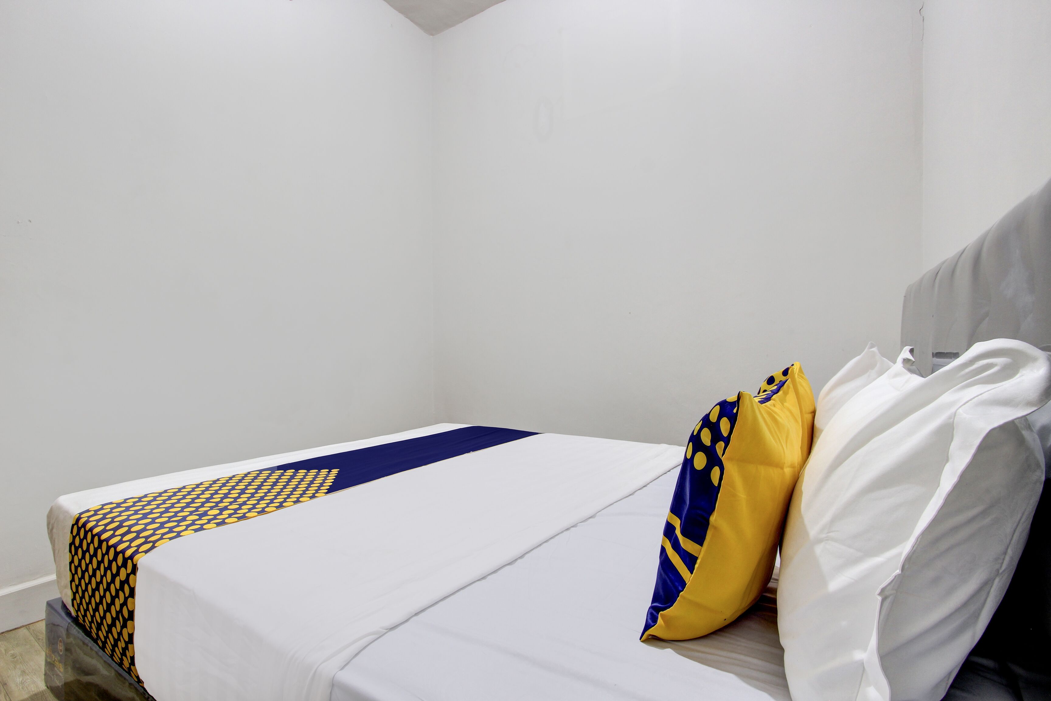 A single bed with a white mattress, a blue and yellow patterned bedspread, and two pillows, one yellow and one white.