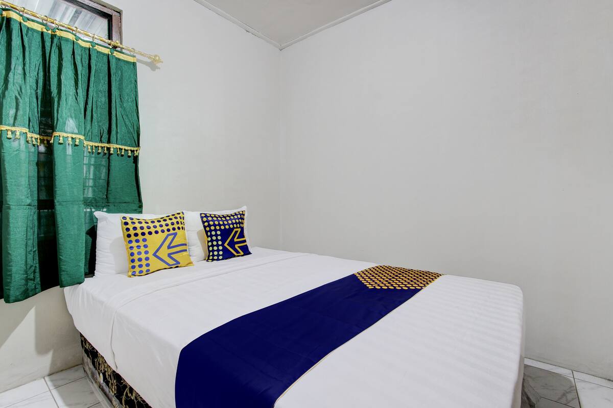 Una cama bien hecha con ropa de cama blanca, dos almohadas estampadas y una manta azul.