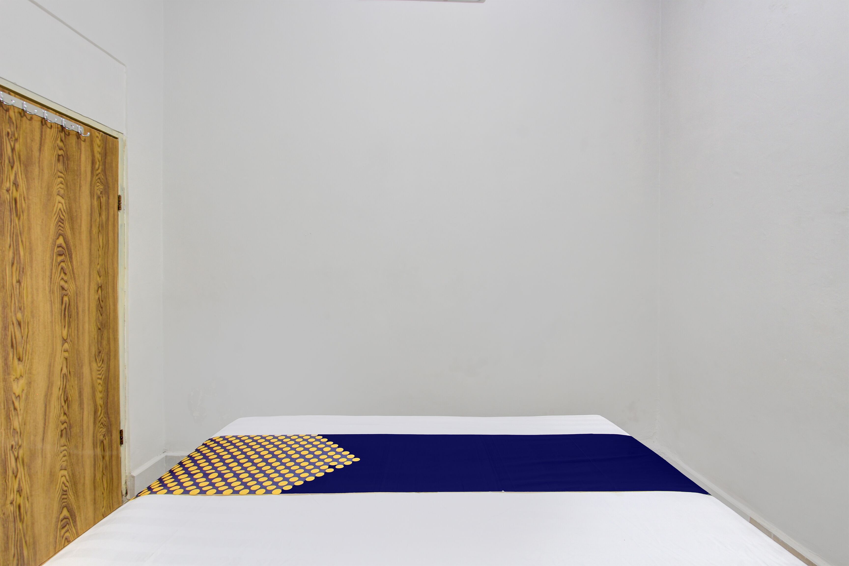 Une petite pièce étroite, avec un lit simple, une porte en bois et des murs blancs unis.
