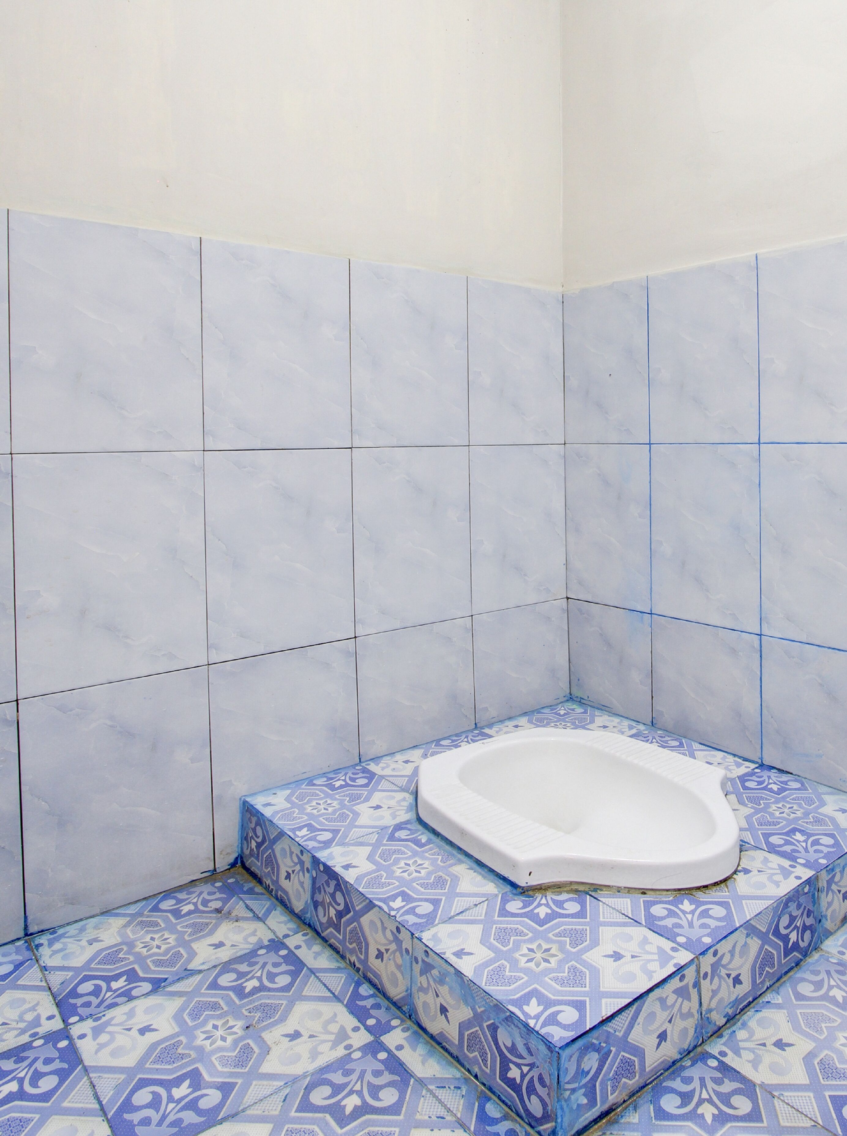 A bathroom with a white bathtub on a blue and white patterned floor, surrounded by white tiles.