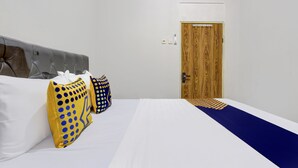 A hotel room with a bed, two pillows, a wooden door, and a white wall. - SPOT ON 93717 Nayus Homestay Syariah 4 (Yogyakarta)