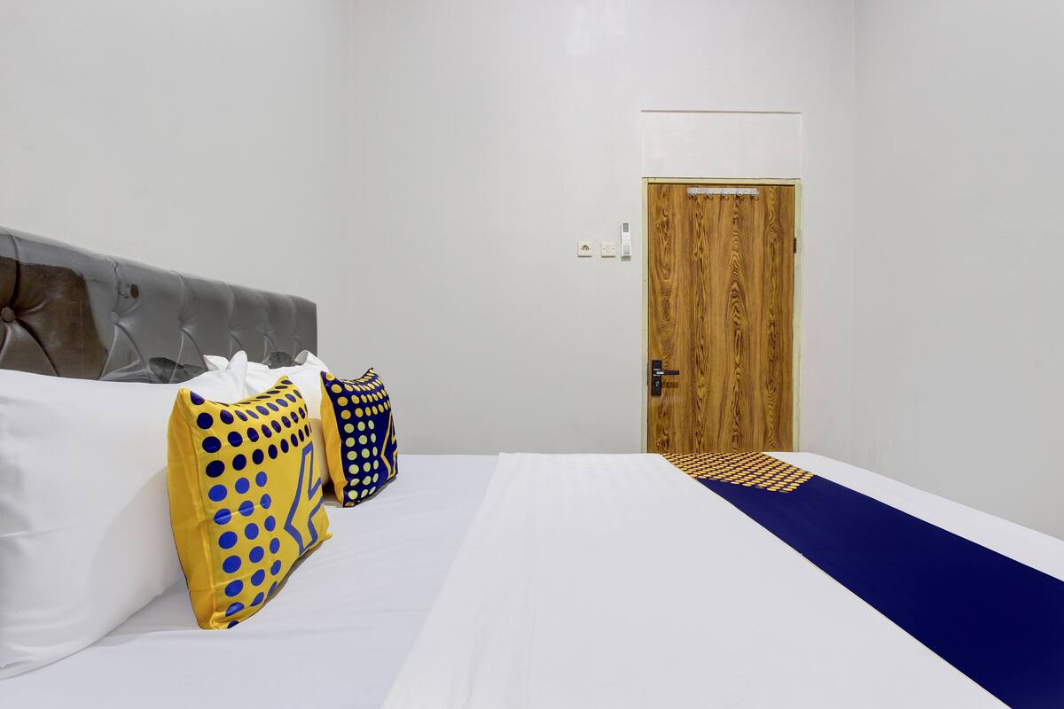 Una habitación de hotel con cama, dos almohadas, una puerta de madera y una pared blanca.