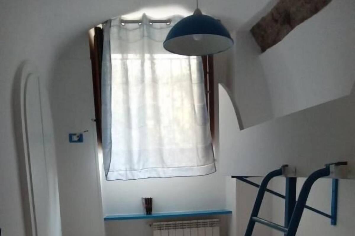 A small, compact room with a bunk bed, a ladder, a window with curtains, and a radiator.
