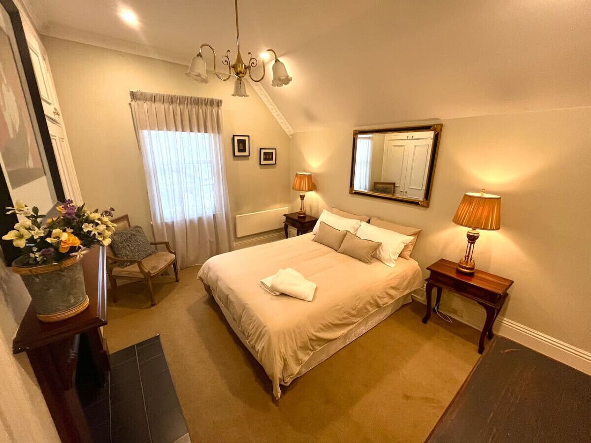 Une chambre à coucher avec un grand lit, deux tables de chevet avec des lampes, une chaise, un miroir et un vase avec des fleurs.