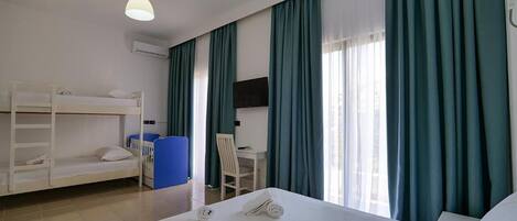 A hotel room with a bunk bed, a desk, a chair, a TV, and a large bed.