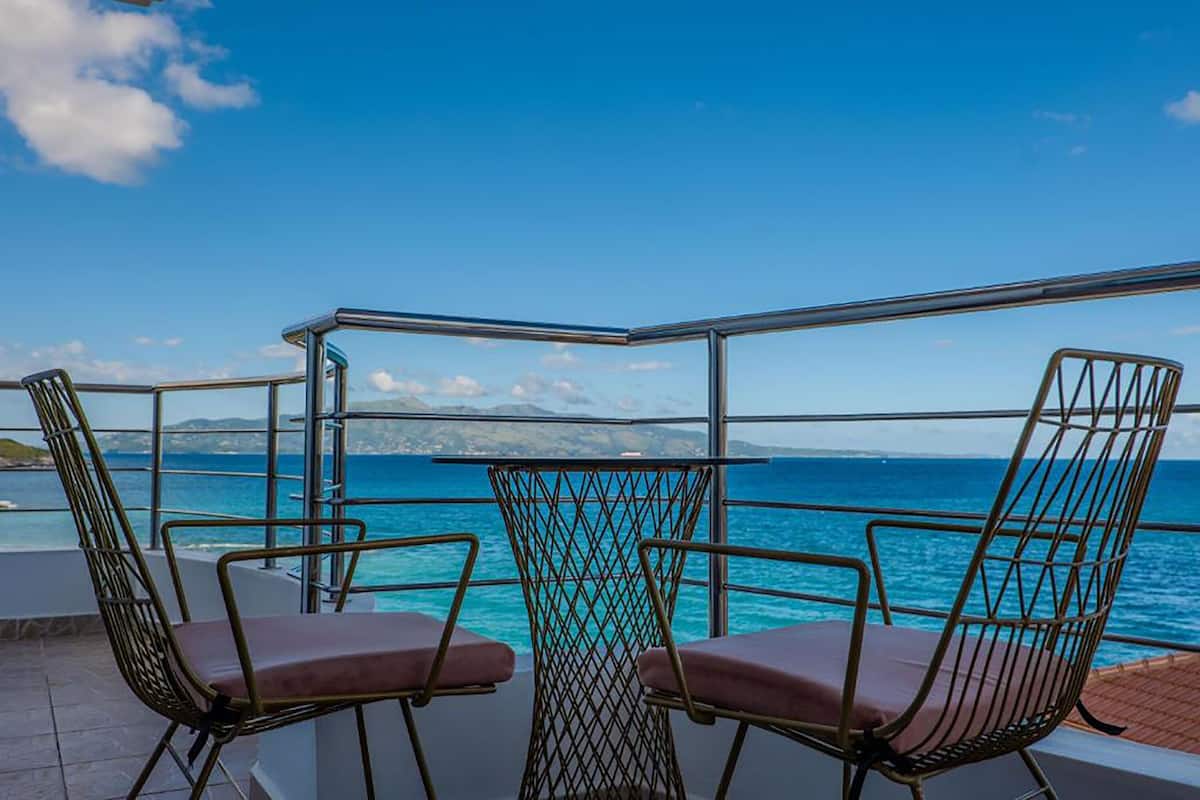 Un balcón con dos sillas y una mesa, con vista a una masa de agua y tierra distante.