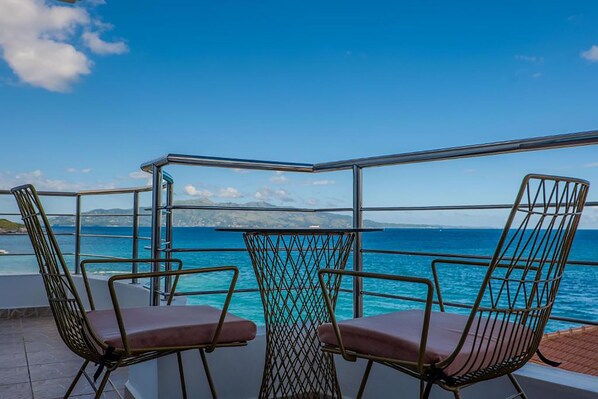 A balcony with two chairs and a table, overlooking a body of water and distant land. - El Mare Hotel (Sarandë)
