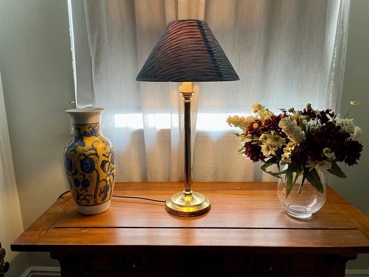 A wooden table with a lamp, a vase, and a bouquet of flowers.