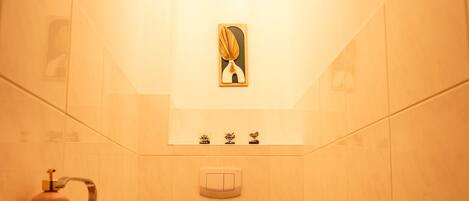 A small, well-lit bathroom with a toilet, sink, and a single shelf with toiletries.
