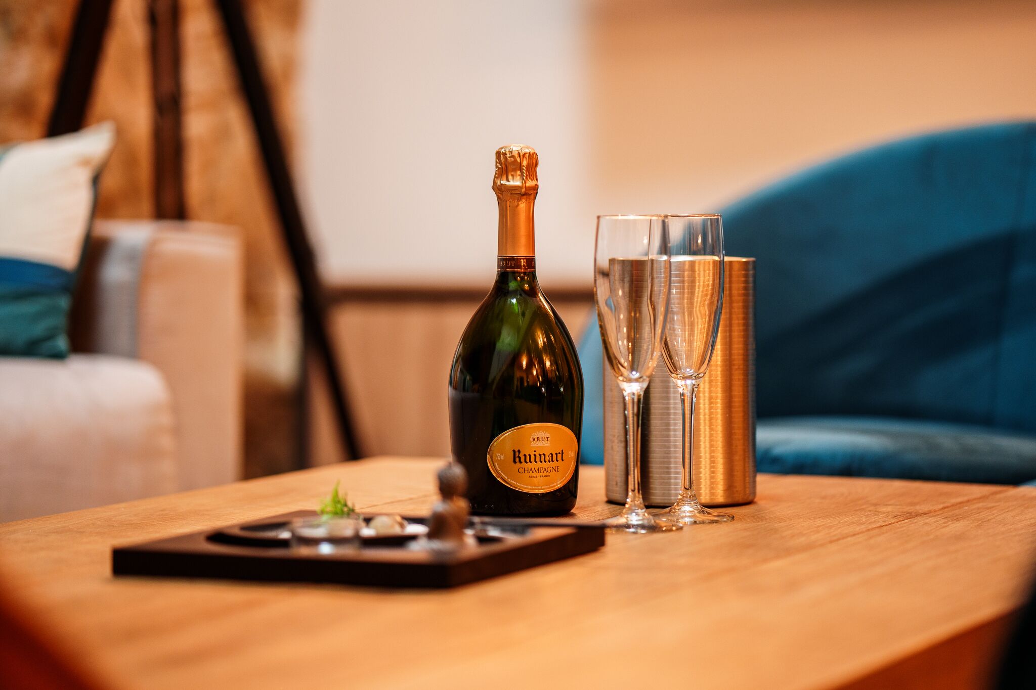 A bottle of Ruinart champagne and two glasses on a wooden table.
