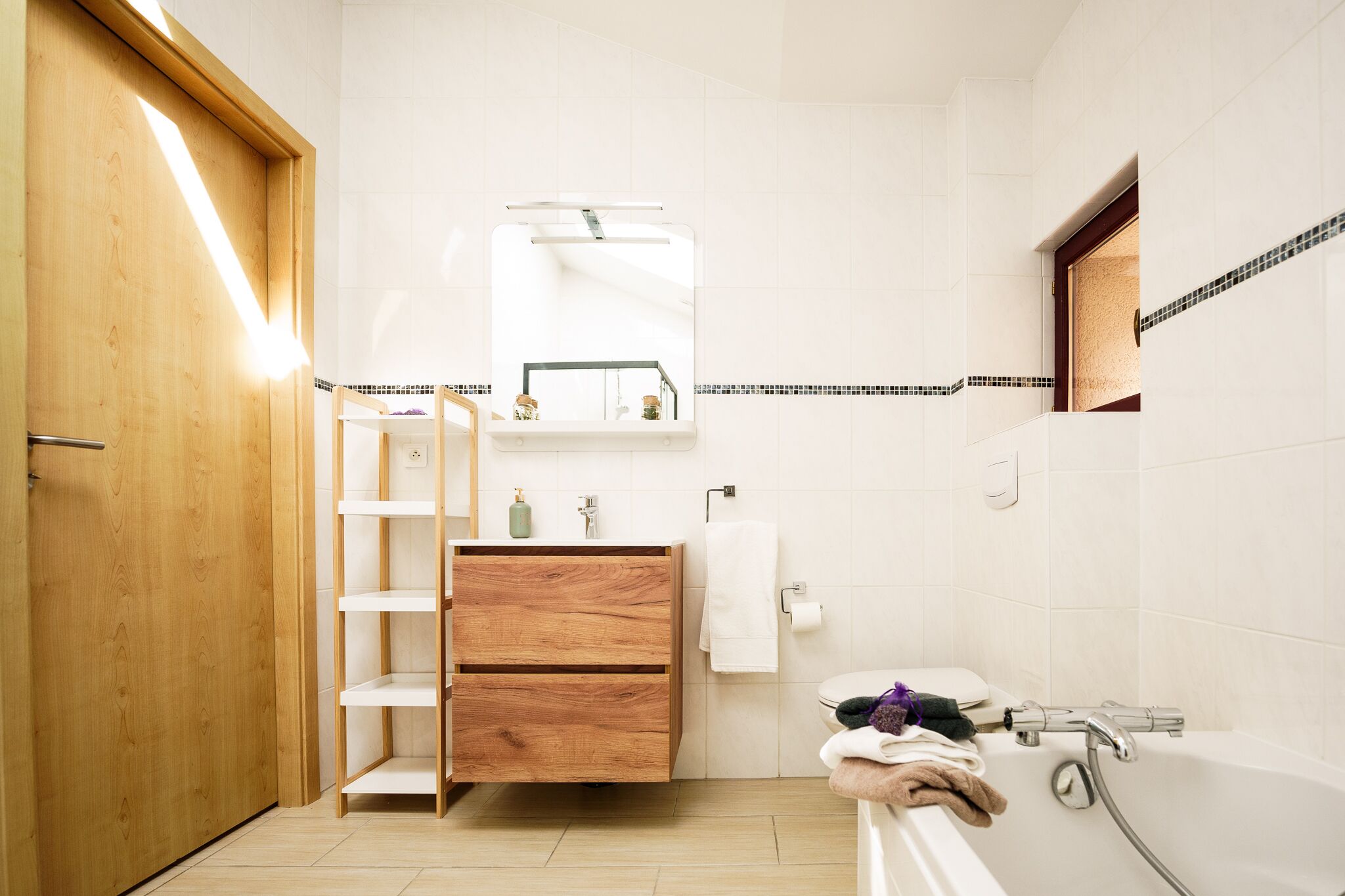 Un bagno moderno con un mobile bagno in legno, un water, una vasca da bagno e uno specchio sopra il lavabo.