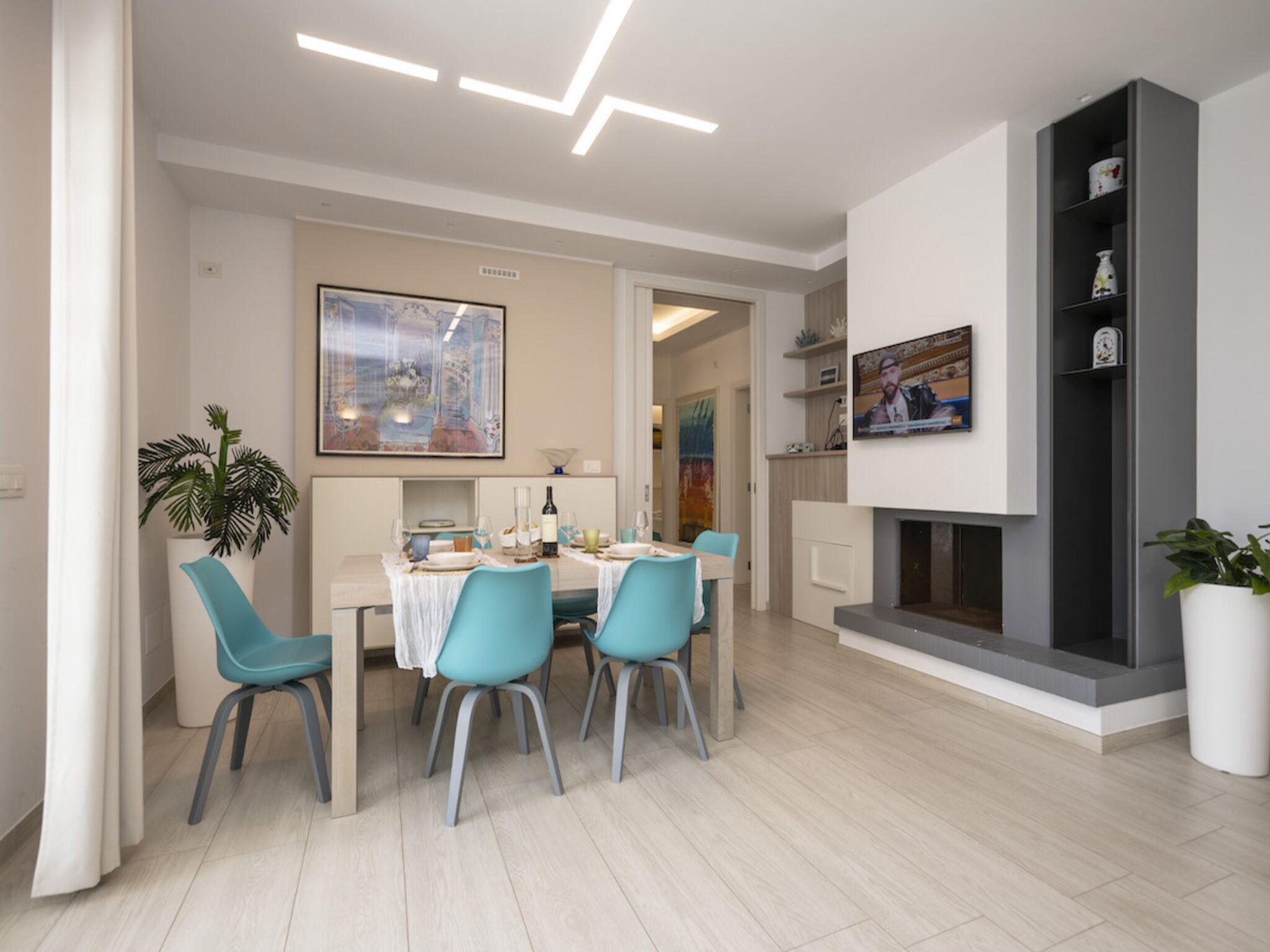 Un comedor moderno con una mesa preparada para cuatro personas, un televisor montado en la pared y una chimenea.
