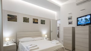 Quarto de hotel moderno com uma cama grande, mesas de cabeceira, televisão e guarda-roupa.
