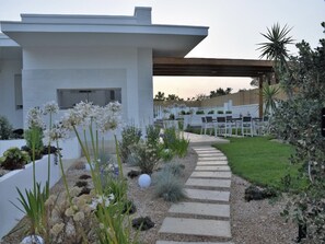 Ein modernes Haus mit einem gepflasterten Weg, der zu einer Terrasse mit Gartenmöbeln führt.
