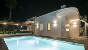 A modern house with a swimming pool, a covered outdoor area, and a staircase leading to an upper level.