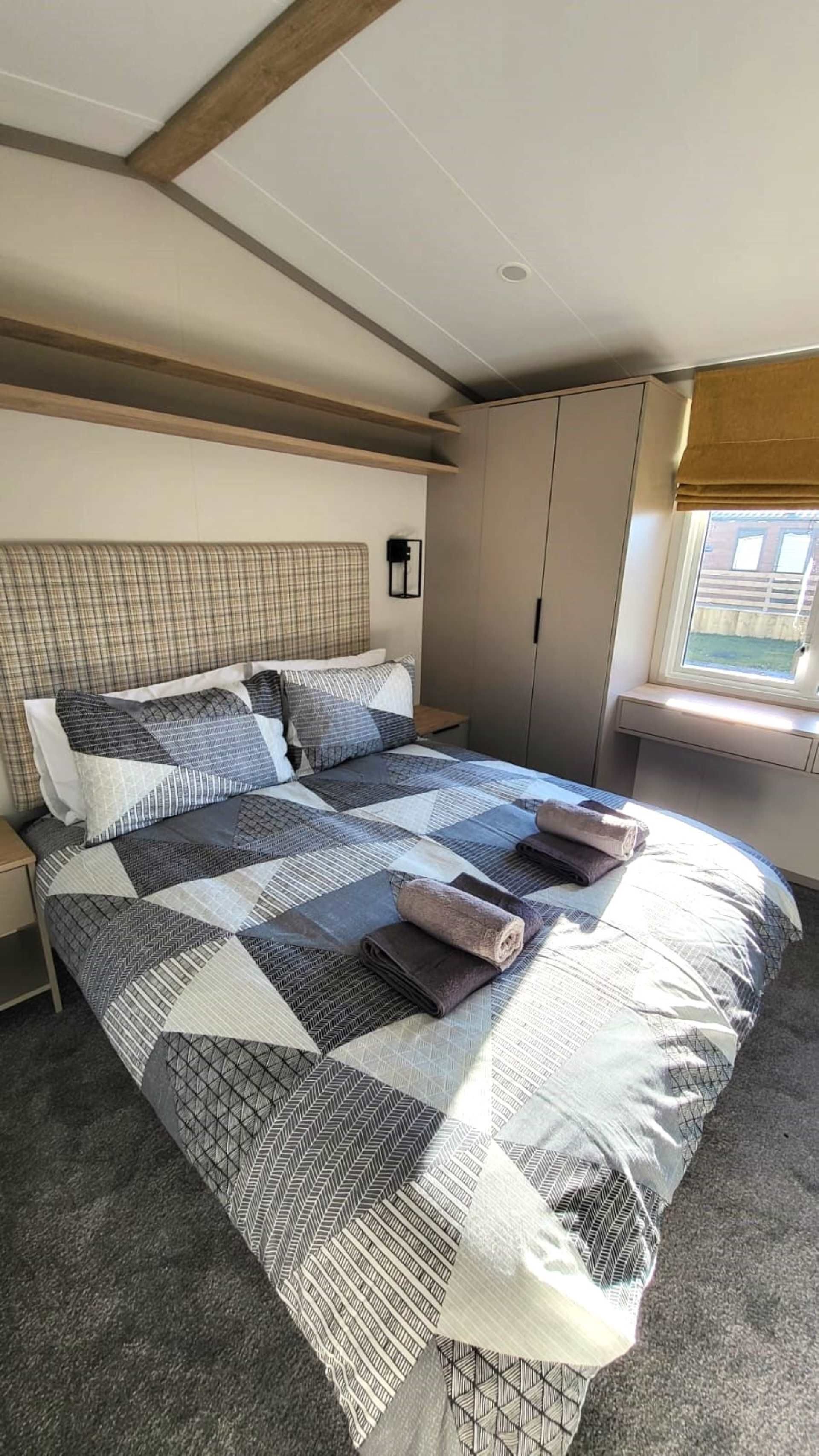 A bedroom with a large bed, a headboard, a wardrobe, a nightstand, and a window with a view of buildings.