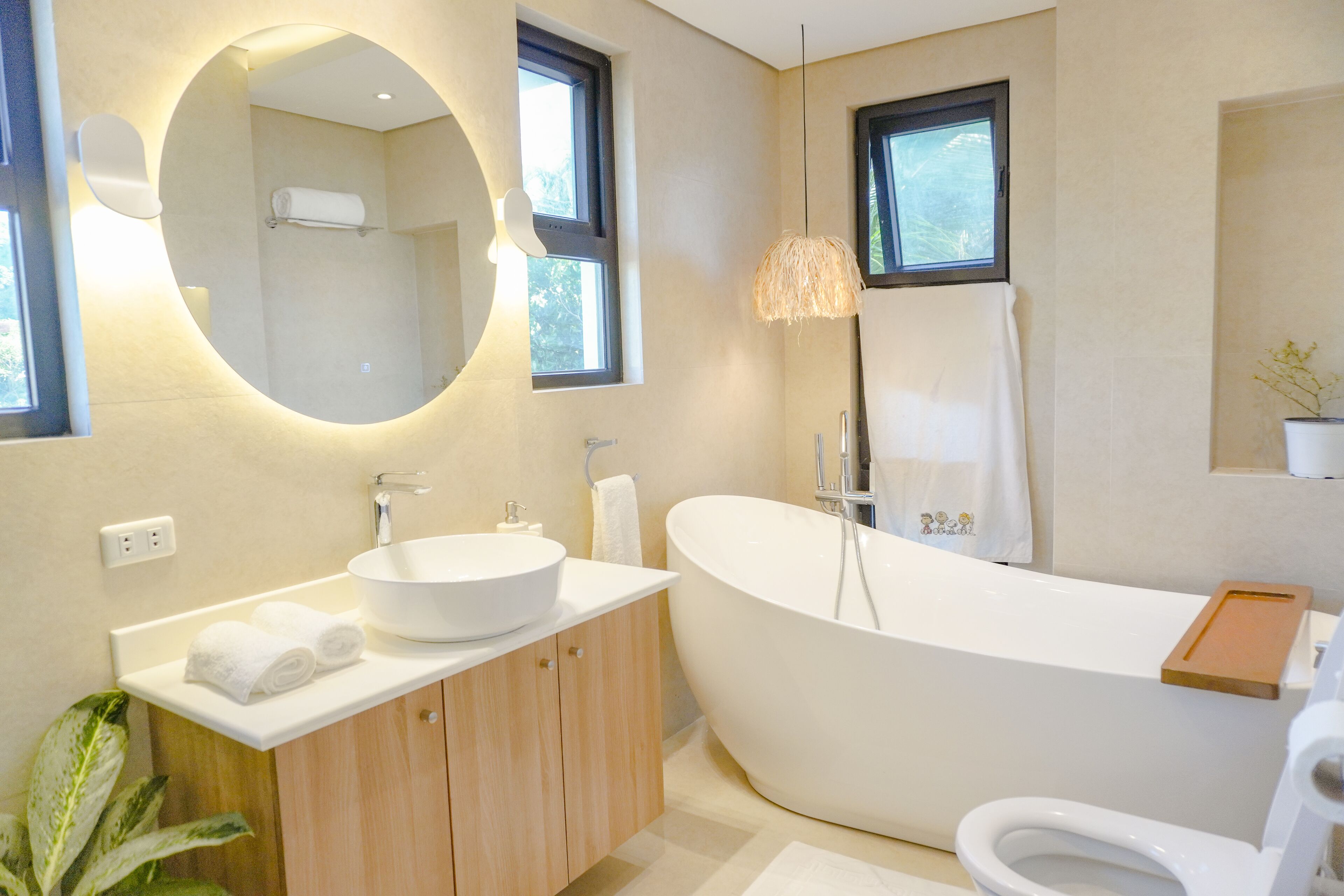 Un baño moderno con una bañera independiente, un espejo redondo y un mueble de tocador de madera.