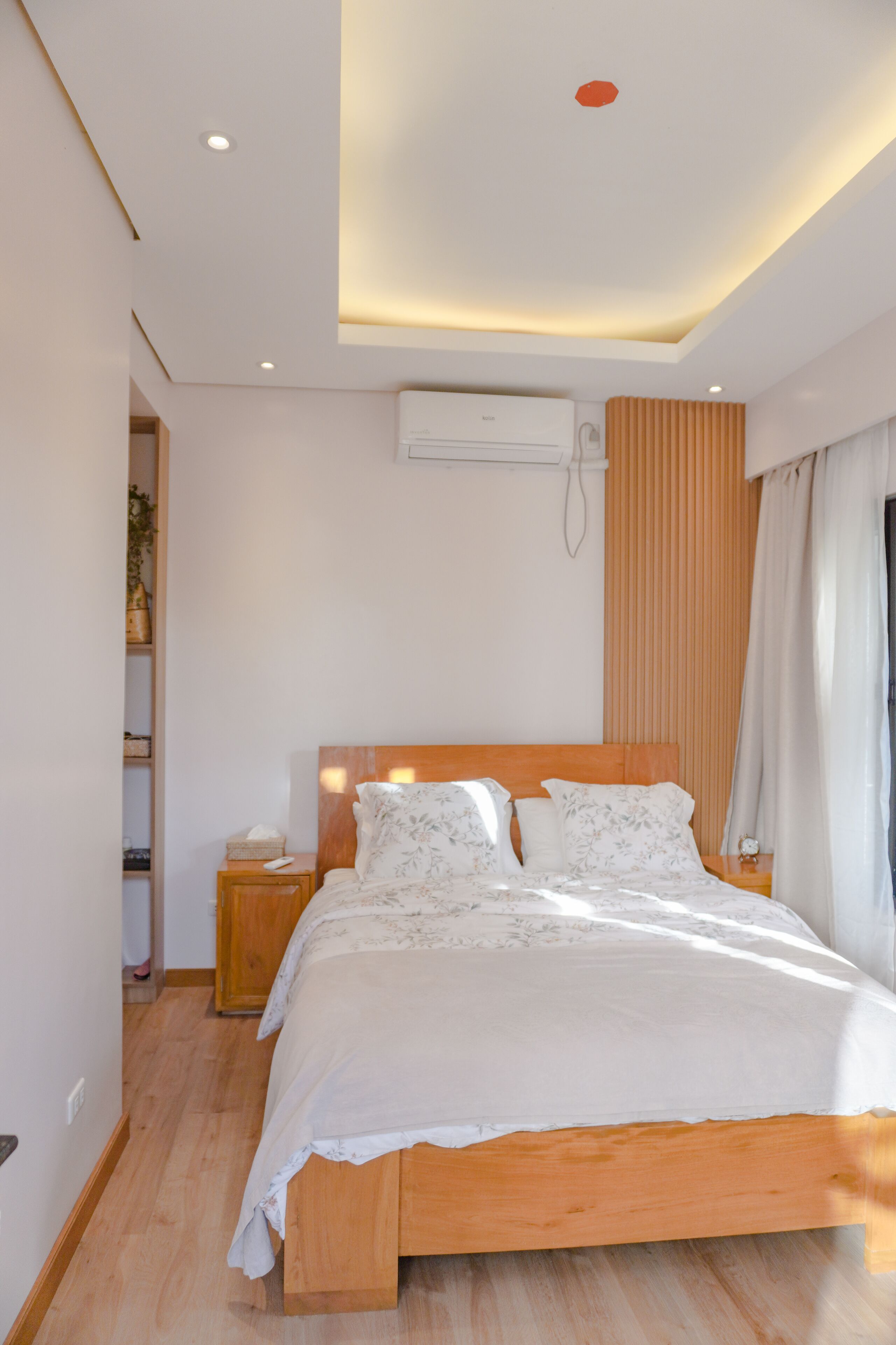 A modern bedroom with a wooden bed, white bedding, a nightstand, and a built-in shelf.